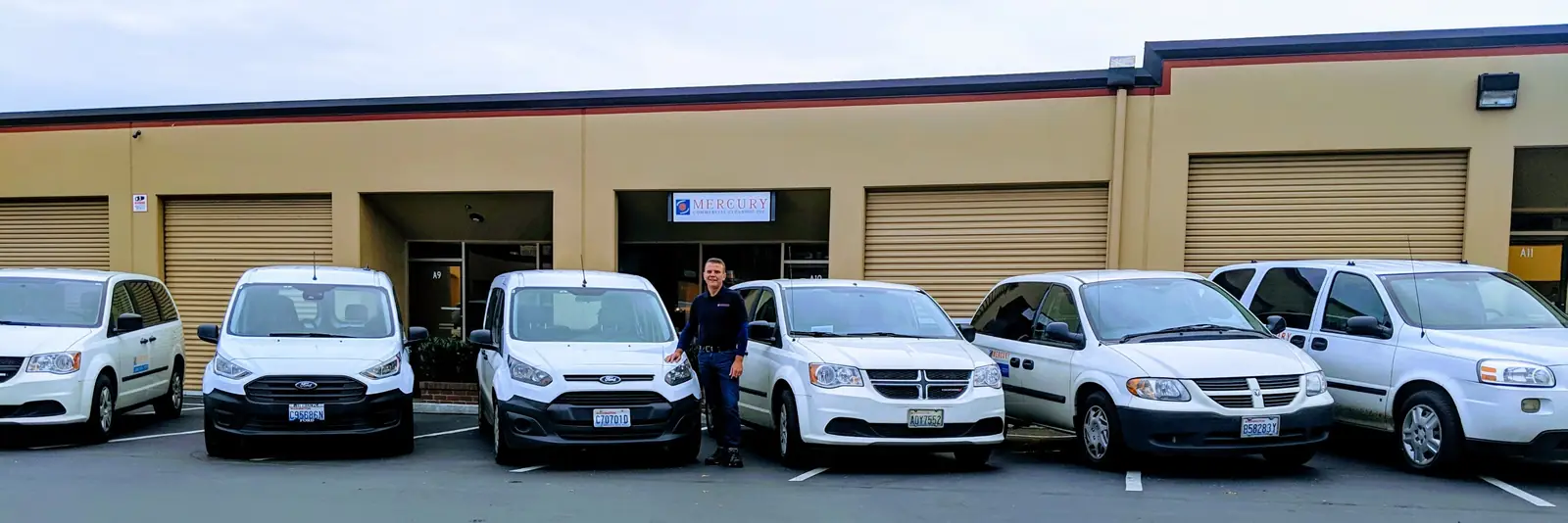 Mercury Commercial Cleaning's unit on S Cloverdale St with its sign above the door and a row of six white vans out front